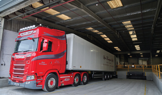 Elye Distribution – Freight Truck at Warehouse Loading Bay Red Scania freight truck positioned at a warehouse loading bay during loading operations.